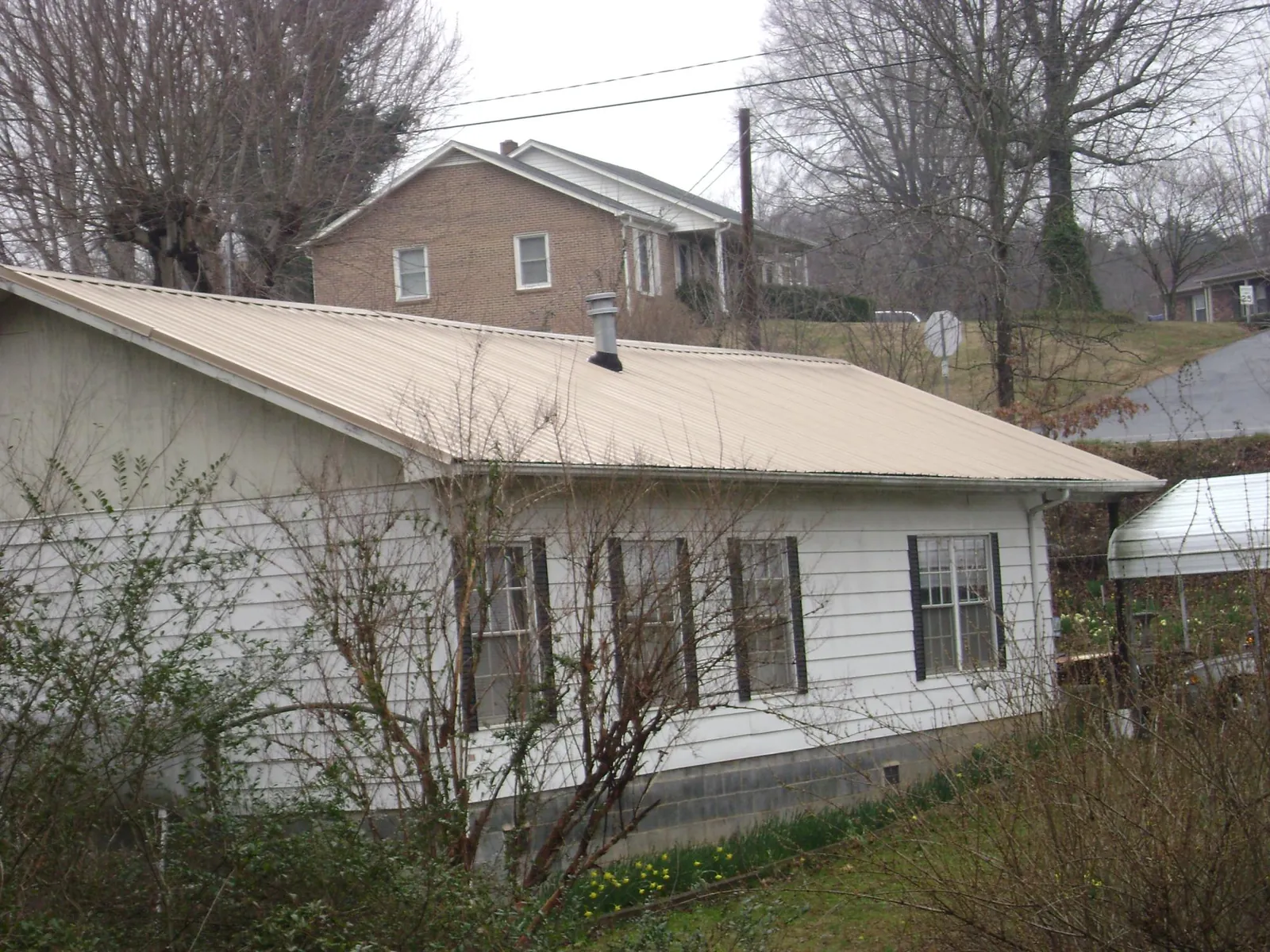 Tan metal roof on a white sided house set into a hillside — Commercial Roofing by Roofing Brothers in Stewartsville
